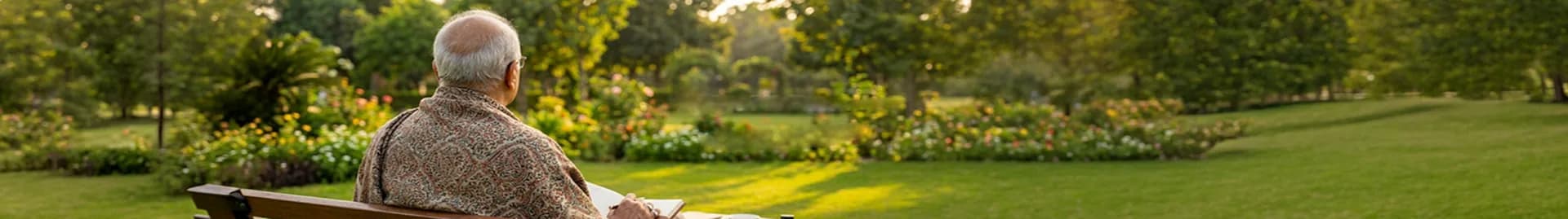 Dr. Zubair sitting on a garden bench with a notebook, looking out over a sunlit lawn